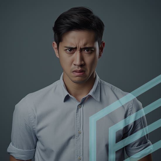 A man with short black hair, wearing a light blue button-up shirt, has an upset expression on his face with furrowed eyebrows and slightly pursed lips. The background is dark gray and there are abstract teal geometric lines overlaying part of the image.