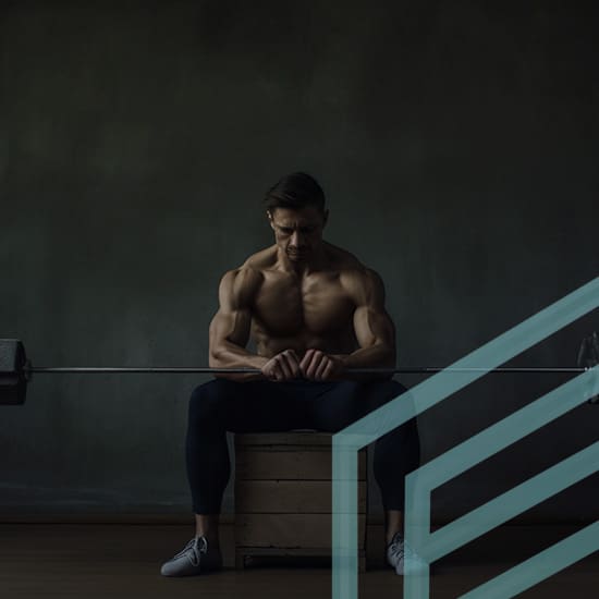 A shirtless man with muscular build sits on a wooden box in a dimly lit gym, holding a barbell across his lap. He appears deep in thought, looking down with a serious expression. Green geometric lines are superimposed over the lower right corner of the image.