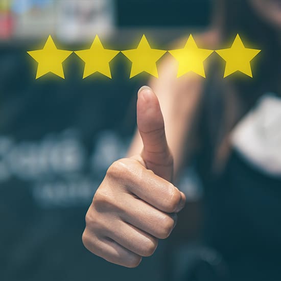 A hand giving a thumbs-up is in the foreground of the image. Above the hand, there are five bright yellow stars aligned horizontally, indicating a five-star rating. The background is blurred and dark, making the hand and stars the focal point.