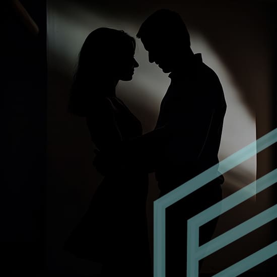 A silhouette of a couple standing close and facing each other in a dimly lit room, creating an intimate and romantic atmosphere. The background is dark with a soft light partially illuminating them from behind. Geometric patterns are visible in the foreground.
