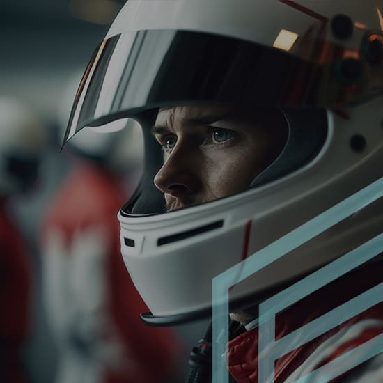 A person wearing a white racing helmet with a reflective visor looks intensely to the side. They are dressed in a red and white racing suit, with a blurred background showing other helmeted individuals. The image is slightly dark with a focused close-up on the person's face.