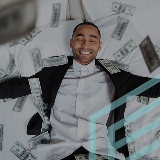 A man in a black suit and white shirt lies on a bed with outstretched arms, smiling with his eyes closed. He is surrounded by scattered hundred-dollar bills. The scene conveys a sense of wealth and relaxation.