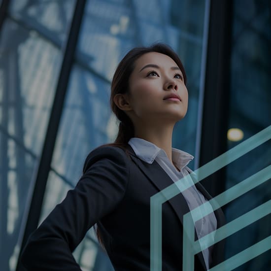 A confident woman in business attire stands with hands on hips, gazing upward thoughtfully. She is outdoors near a modern glass building, reflecting light. The image conveys ambition and determination.