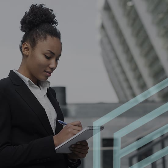 A person with natural hair in a bun, dressed in a black blazer and white shirt, is writing in a notebook while standing outside. There is a modern, glass building in the background, and geometric designs overlay the image.
