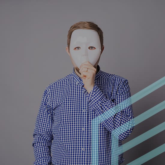 A person wearing a blue and white checkered shirt holds a white mask in front of their face, obscuring their identity. The background is gray, and there are diagonal teal lines in the lower right corner of the image.