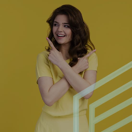 A woman with wavy brown hair wearing a yellow shirt stands against a yellow background. She is smiling and pointing both of her index fingers in opposite directions while crossing her arms in front of her chest. Transparent geometric lines overlay the image.