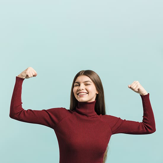 A young woman with long brown hair and a red turtleneck sweater smiles while flexing both arms, showcasing her biceps. The background is a solid light blue.