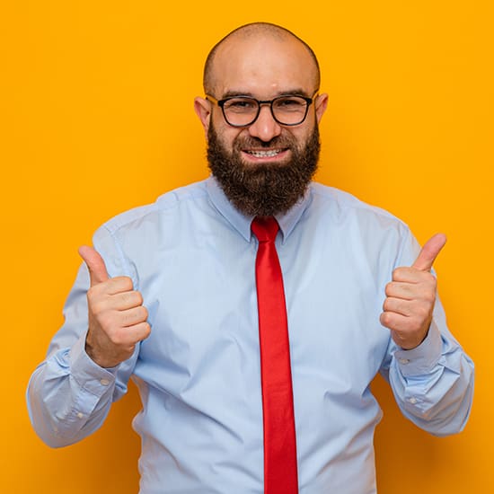 A bald man with a bushy beard, wearing glasses, a light blue dress shirt, and a red tie stands against an orange background, giving two thumbs up with a cheerful expression.