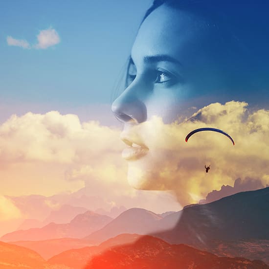 A double exposure image features a woman's calm face superimposed with a vibrant sunset sky and mountainous landscape. A paraglider soars through the sky, blending seamlessly with the scene, creating a dreamlike and inspiring visual.