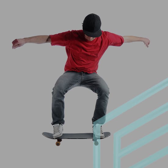 A person wearing a red shirt, jeans, and a black cap is performing a skateboard trick in mid-air against a grey background. There are light blue geometric shapes overlaying the lower right side of the image.